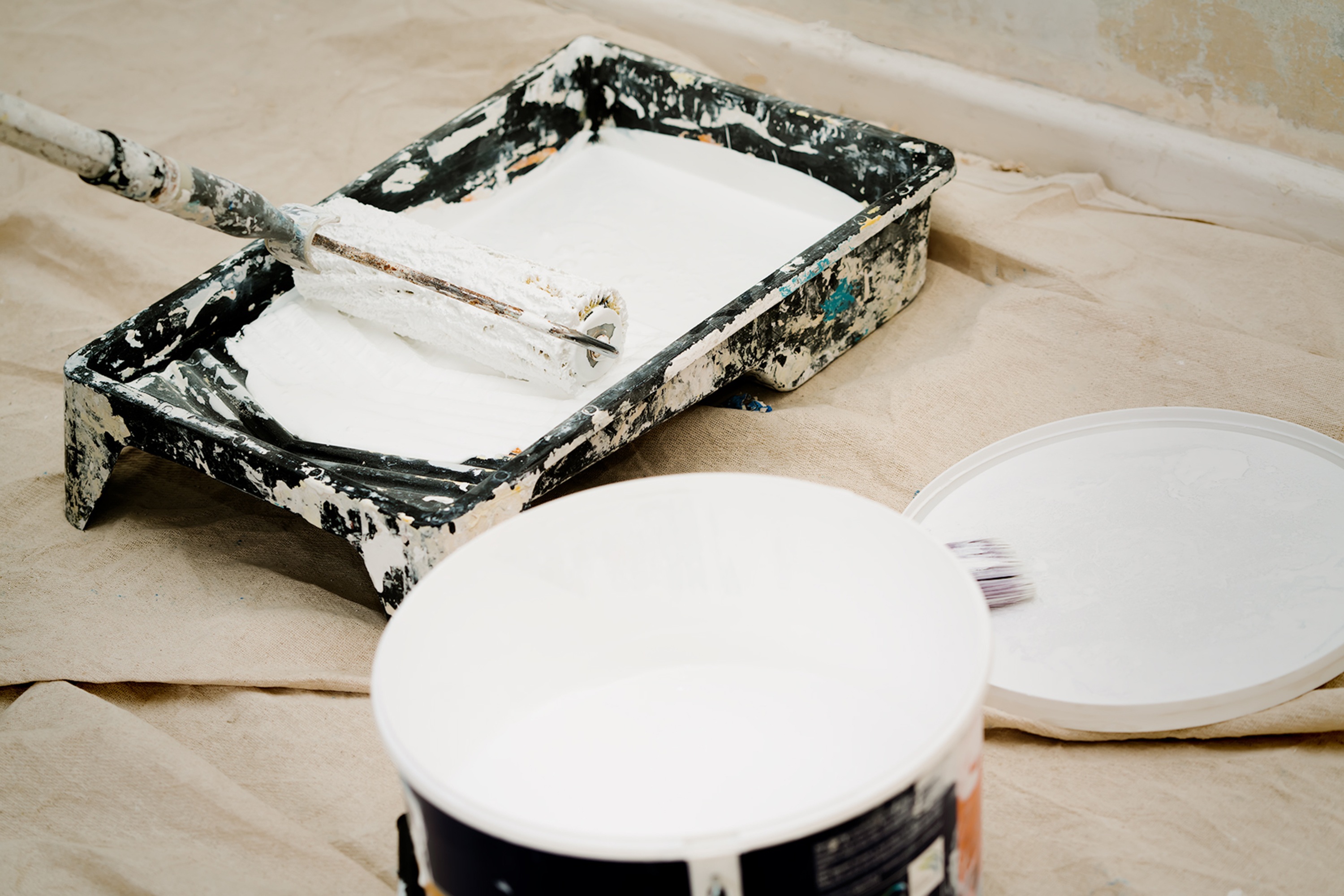 Roller, tray and open tin of paint on a drop sheet